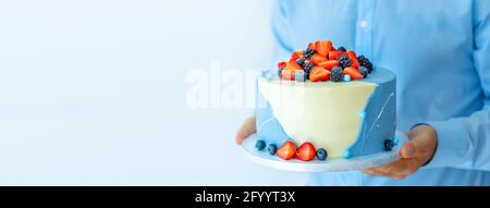 Ein Mann Gebäck Shef hält einen schönen großen Kuchen mit Beeren in den Händen. Männlicher Koch kocht Konditor oder Bäcker. Modell „Copy Space Food“-Konzept Stockfoto
