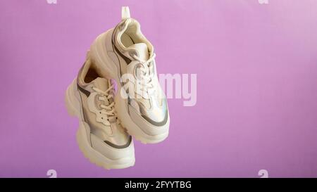 Weiße Sneaker fliegen an der lila Wand. Weibliche weiße Lederschuhe auf violettem Hintergrund. Paar stylische urbane Sneaker. Bequemer Sportswear-Hipster Stockfoto