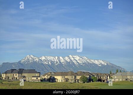 Aufnahme von Häusern nebeneinander mit einem grasbewachsenen Platz vorne und Bergen im Hintergrund. Stockfoto