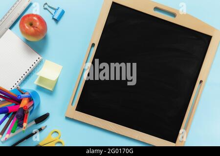 Flat Lay mit Schulkonzept auf blauem Hintergrund mit verschiedenen Schulzubehör, Stiften, Bleistift, Notizblock, Büroklammern, apfel, Lineal, Schere, leer Stockfoto