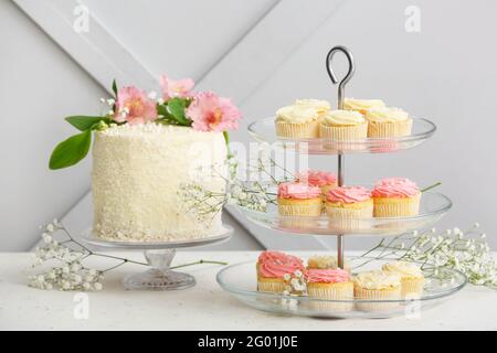 Dessertständer mit leckeren Cupcakes, Kuchen und Blumen auf dem Tisch Stockfoto