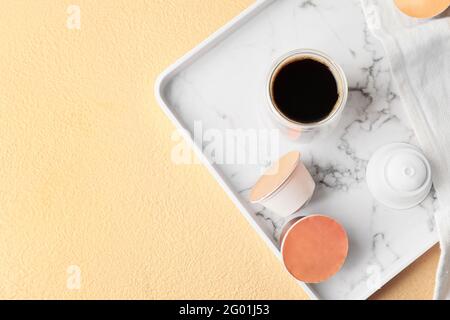 Tablett mit Glas Kaffee und Kapseln auf dem Tisch Stockfoto