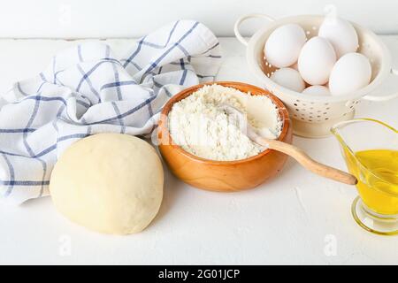 Schüssel mit frischem Teig, Mehl, Eiern und Öl auf hellem Hintergrund Stockfoto