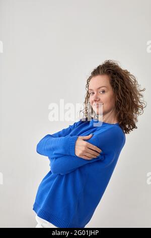 Seitenansicht des Inhalts Frau trägt trendigen blauen Pullover stehend Auf grauem Hintergrund im Studio und Blick auf die Kamera Stockfoto