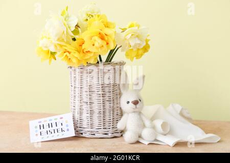Schöne Narzissen Blumen, Spielzeug und Karte mit Text HAPPY EASTER auf farbigem Hintergrund Stockfoto