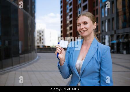 Business stilvolle Frau in einer blauen Jacke hält ein Abzeichen In der Hand vor dem Hintergrund eines Bürogebäudes Stockfoto