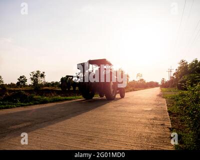 Blauer Traktor auf der Straße nach der Arbeit auf dem Bauernhof bei Sonnenuntergang. Silhouette eines alten Traktors auf der Landstraße auf dem Weg nach Hause. Stockfoto