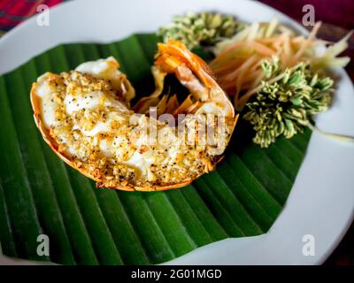 Gegrillte Hummerschwänze in Knoblauchbutter serviert auf einem grünen Bananenblatt auf einem weißen Gericht, köstliche Meeresfrüchte im thailändischen Stil. Stockfoto