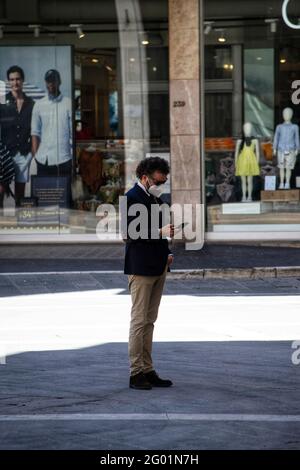 Arezzo, Italien, 28. Mai 2021, ein Geschäftsmann mit medizinischer Maske überprüft sein Handy vor einem Schaufenster voller Schaufensterpuppen Stockfoto