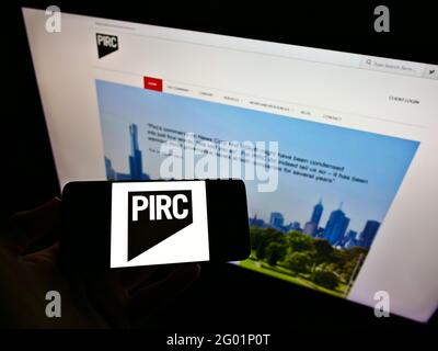 Person mit Mobiltelefon und Logo von Pensions and Investment Research Consultants (PIRC) auf dem Bildschirm vor der Webseite. Konzentrieren Sie sich auf die Telefonanzeige. Stockfoto
