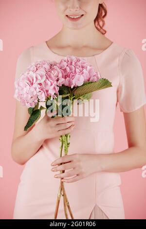 Zugeschnittenes Bild einer lächelnden Frau mit rosa Hortensien Stockfoto