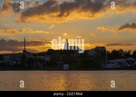 Die Küste der Stadt am Abend des Sonnenuntergangs.Sonnenstrahlen, die durch Sturmwolken über der Stadt der Bucht des Sees hindurchziehen. Stadtbild.Goldene Stunde. Stockfoto