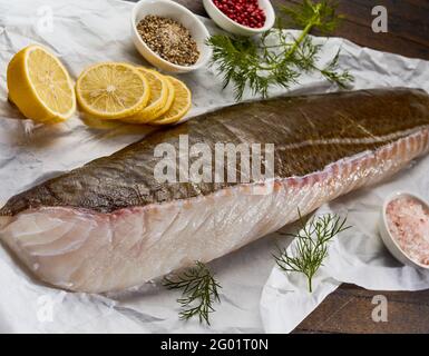 Von oben aus frischem rohem Kabeljaufischfilet Papier mit verschiedenen aromatischen Zutaten für die Marinade vor dem Kochen Holztisch Stockfoto