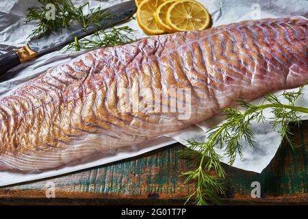 Von oben rohes pollock Fischfilet mit frischem Dill Und Zitrone auf Schneidebrett mit Messer während der Lebensmittelzubereitung Stockfoto