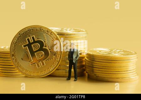 Stapel Bitcoins mit Miniatur-Geschäftsmann auf goldenem Hintergrund. Kryptowährungskonzept. Stockfoto
