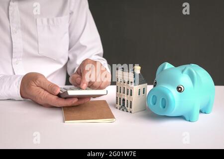 Geschäftsmann mit Rechner mit einem Modellhaus und Sparschwein auf dem Tisch. Kauf von Immobilien oder Hypothek Konzept. Stockfoto