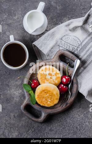 Frühstück Essen Lecker Konzept. Hüttenkäse-Pfannkuchen, Syrniki, Quark-Fritten mit Kirsche auf dunklem Beton-Tischhintergrund. Draufsicht Stockfoto
