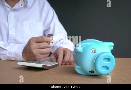 Geschäftsmann hält eine Münze im Hintergrund mit Fokus auf Sparschwein, der an der Seite liegt. Brach- oder Finanzkrisenkonzept. Stockfoto