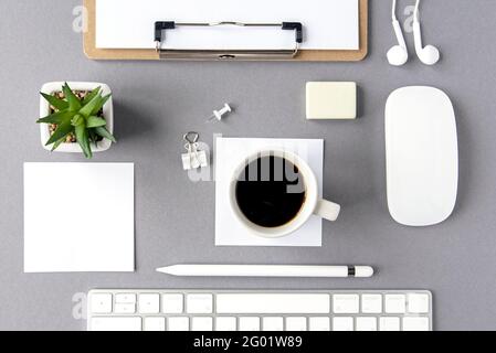Flache Laie mit minimaler weißer Zusammensetzung. Business Workplace. Tastatur, leeres Blatt, Stift, Kopfhörer, Pflanze, Kaffeetasse auf hellgrauer Oberfläche als Modell Stockfoto