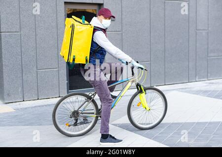 Ein junger Kurier liefert Essen mit einem gelben Thermalrucksack und fährt mit dem Fahrrad in der Stadt. Konzept für den Lieferservice von Lebensmitteln Stockfoto