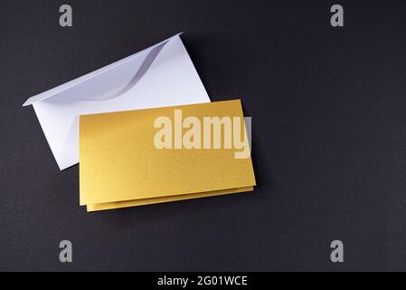 Weißer Umschlag und Einladung als goldenes Quadrat mit leerer Oberfläche auf schwarzem Hintergrund, Mockup, Platz für Text Stockfoto