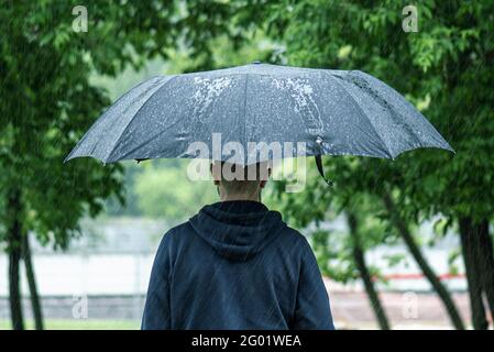 Allein Mann, der mit schwarzem Regenschirm bei starkem Sommerregen an einem regnerischen Tag in einem Stadtpark läuft, Konzept Wetter Bild Stockfoto