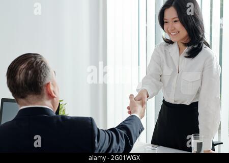 Hübsche junge Geschäftsfrau, die zuvor die Hände des Abteilungsleiters schüttelte Besprechung oder Vorstellungsgespräch Stockfoto