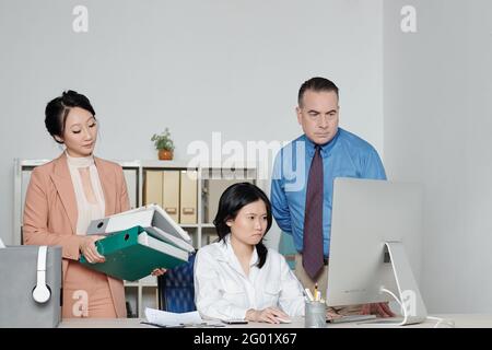 Frustrierte junge Geschäftsfrau, die bei ihren Kollegen auf den Computerbildschirm schaut Mehr Arbeit für sie Stockfoto