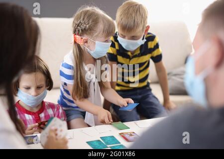 Kinder und Erwachsene spielen Brettspiele in schützenden medizinischen Masken Stockfoto