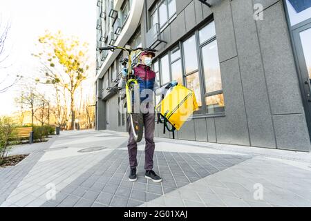 Ein junger Kurier liefert Essen mit einem gelben Thermalrucksack und fährt mit dem Fahrrad in der Stadt. Konzept für den Lieferservice von Lebensmitteln Stockfoto