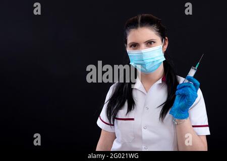 Medizin, Impfung und Gesundheitskonzept, Nahaufnahme der Ärztin in Gesichtsmaske mit Stethoskop und Spritze über dunklem Hintergrund Stockfoto