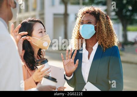 Lächelnde junge Geschäftsfrau in Schutzmaske im Gespräch mit Kollegen, wenn Tagungen im Freien Stockfoto