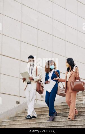 Gruppe von Mitarbeitern in Schutzmasken tragen Klemmbretter und reden Wenn man die Treppe im Freien hinuntergeht Stockfoto