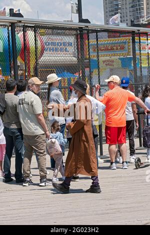 Ein Mann, der behauptet, Buddhist zu sein, bietet Bücher und Armbänder an und bittet um Spenden. Auf dem Boardwalk in Coney Island, Brooklyn, New York. Stockfoto