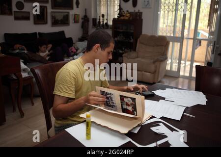 Der 22-jährige junge Mann ist SMS mit seinem Handy, er dreht Seiten eines Familienalbums, während er zu Hause im Wohnzimmer sitzt und studiert. Stockfoto