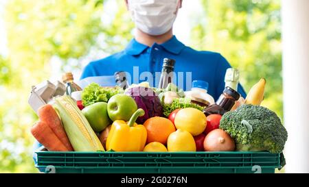 Deliveryman trägt Gesichtsmaske hält Lebensmittelkorb im Freien, hygienische Lebensmittel-Lieferservice in der Zeit der Pandemie-Konzept Stockfoto