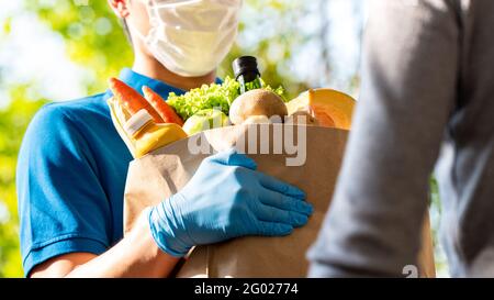 Hygienischer Lieferer, der Gesichtsmaske und Gummihandschuhe trägt, während er Lebensmittel an den Kunden zu Hause liefert, und die Lieferung von Lebensmitteln in der Zeit der Pandemie Stockfoto