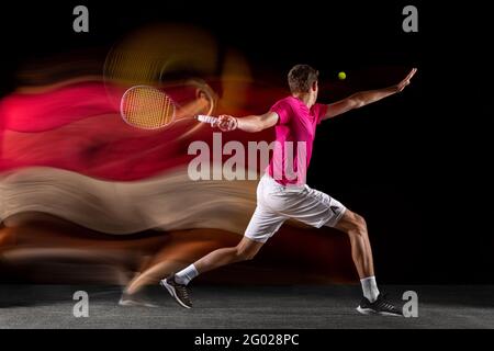 Junger kaukasischer männlicher Tennisspieler, der in gemischtem Licht auf dunklem Hintergrund Tennis spielt. Rückansicht Stockfoto