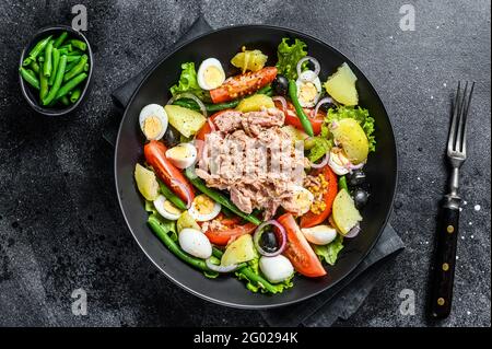 Thunfischsalat mit Gemüse, Eiern und Sardellen auf einem Teller. Schwarzer Hintergrund. Draufsicht Stockfoto