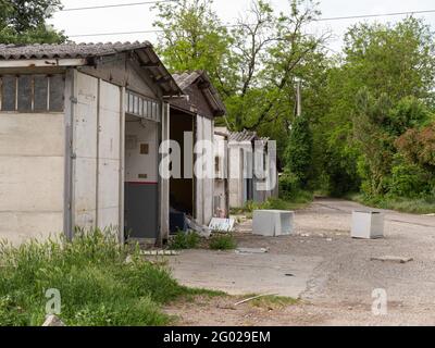 Verfallene kleine Häuser zwischen den Bäumen und der Vegetation und Dump von alten Geräten. Stockfoto