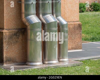 Drei große vertikale Stahlrohre, die an der Außenwand eines Gebäudes befestigt sind. Stockfoto