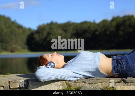 Seitenansicht Porträt einer Frau, die entspannt Musik hört Mit kabellosen Kopfhörern in einem See in den Bergen Stockfoto