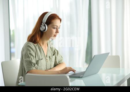 Geballte Frau mit kabellosen Kopfhörern, die zu Hause den Laptop überprüft Stockfoto