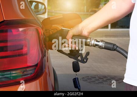 Tankstellenpumpe. Pumpen von Benzin in einem orangefarbenen Auto an einer Tankstelle. Zum Befüllen des orangefarbenen Fahrzeugs mit Kraftstoff in der Tankstelle. Sonnenlicht. Stockfoto