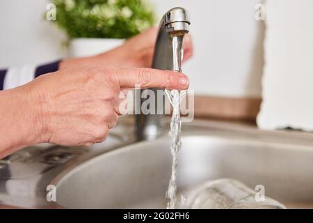 Finger unter fließendem Wasser am Wasserhahn des Sink überprüft das heiße Wasser Stockfoto