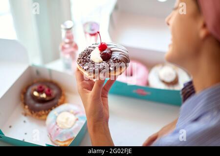 Ein wunderschönes Mädchen in angenehmer Atmosphäre in einer Konditorei ist von dem köstlichen Donut, den sie in der Hand hält, begeistert. Konditorei, Dessert, süß Stockfoto