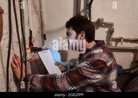 Handwerker oder Handwerker prüft die Installation von Kabeln und Rohren Im Keller Stockfoto