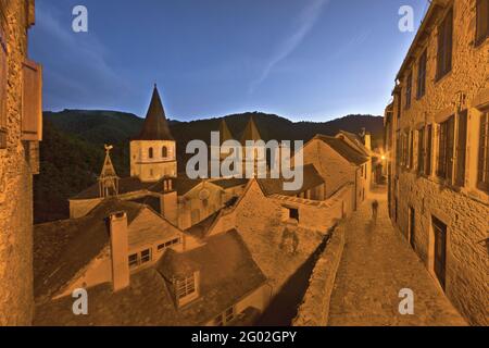 FRANKREICH - AVEYRON - 12 - CONQUES : DIE ABTEIKIRCHE VON SAINTE FOY IN DER ABENDDÄMMERUNG VON DER HAUPTSTRASSE AUS GESEHEN. IN DIESER STELLE VON SELTENER SCHÖNHEIT, WO WILDNIS Stockfoto