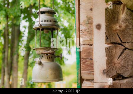 Alte, kaputte und rostige Öllampen, die in der Nähe der alten Holzwand hängen. Litauisches Dorf in der Sommersaison Stockfoto