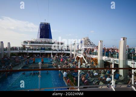 Kreuzfahrtschiffe Azura und Britannia in Antigua Karibik Pool Party Segeln Segeln Abschied Leute Schwimmbad Trichter Sonnenliegen Stockfoto